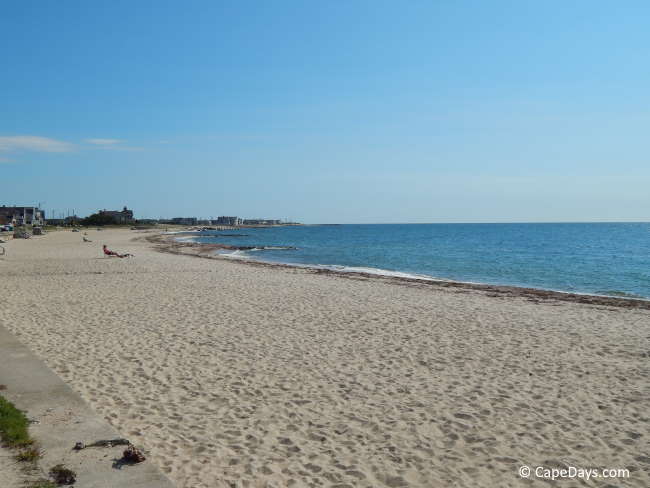 Nearly empty beach, clear sky and blue water, buildings in the distance