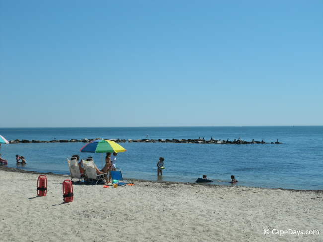 Children playing in the water, family sitting on the beach, jetty in the background