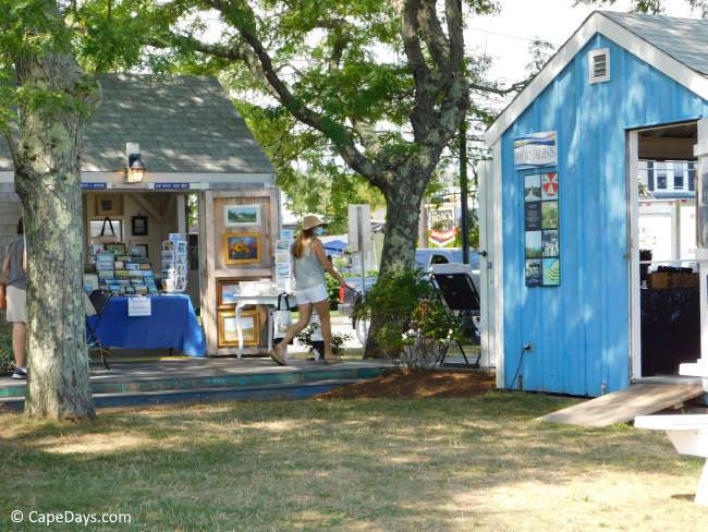 Small, brightly colored artist shanty buildings in a tree-shaded area