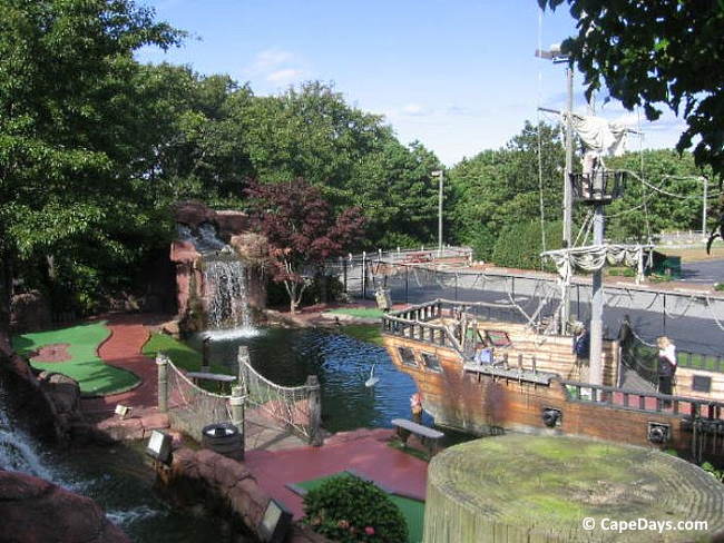 Portion of a mini-golf course showing a pirate ship, waterfall, and a short bridge over a water feature.