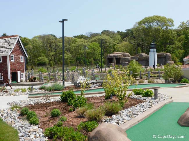 Shingled building, lighthouse, waterfall, shrubbery, and putting greens at Bud’s Mini Golf in Harwich Port.