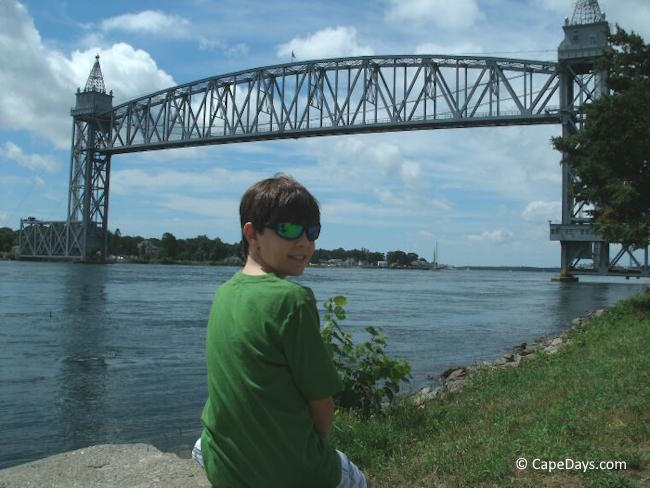 Boy sitting on a rock by the Cape Cod Canal waiting to see the railroad bridge lower for a train crossing