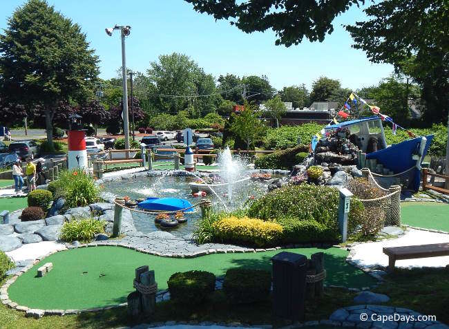 Mini golf course on Cape Cod with landscaped putting greens, water features, and nautical-themed obstacles under a blue sky.