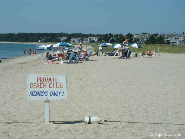 Private beach club sign on a Cape Cod beach with people sitting on the sand behind it