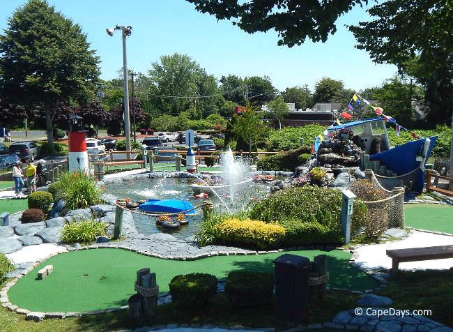 Cape Escape Mini Golf in Orleans with large blue boat, lighthouse, and central water fountain surrounded by flowers