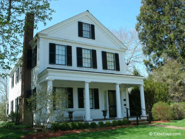 Stately white sea captain's home with black shutters, shaded by trees on either side