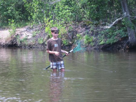Young boy standing in the water with a net in hand, fishing for blue claw crabs