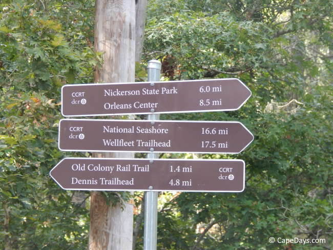 Directional signs along the Cape Cod Rail Trail showing distances to Nickerson State Park, Orleans Center, the National Seashore, Wellfleet Trailhead, the Old Colony Rail Trail, and Dennis Trailhead.