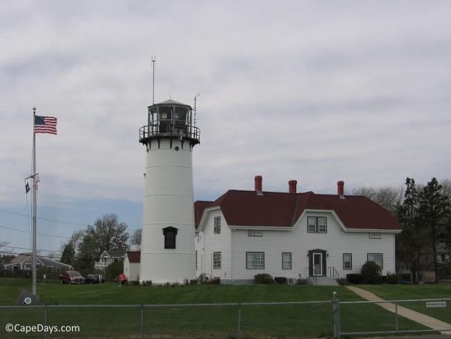 View of the grounds of Chatham Lighthouse, tower and US Coast Guard building, American flag flying from tall flagpole