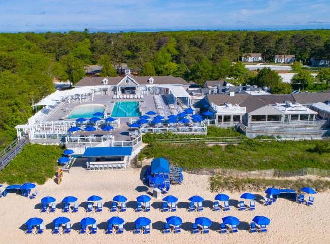 Aerial view of large resort showing pool, beach with beach chairs and umbrellas, and resort buildings