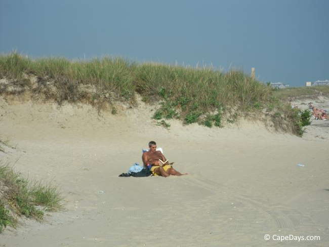 Man sitting in lounge chair, reading a book, in a secluded spot on a sandy beach