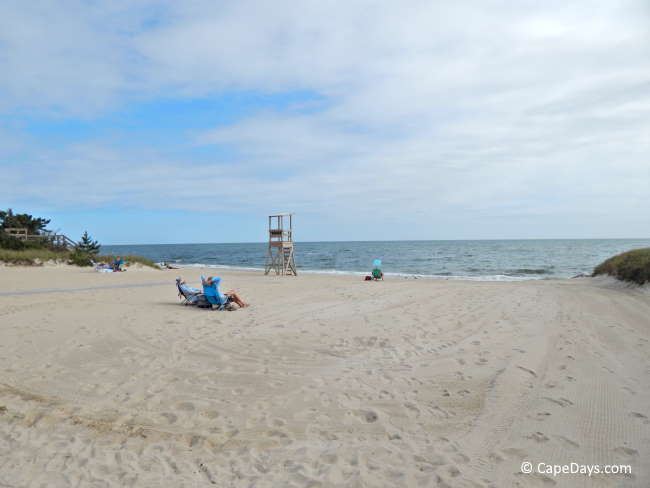 A few beachgoers sitting in their lounge chairs, looking out toward the ocean, small waves rolling in on the shoreline