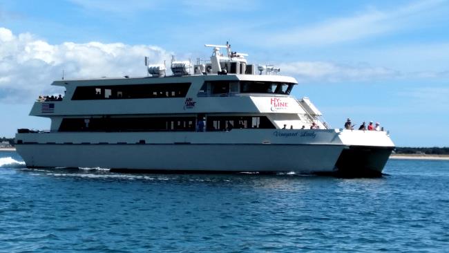 View of passengers on the outer decks of a large, white, dual-hulled ferry boat cruising along lightly rippled water