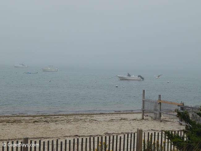Boats moored offshore, blanketed by incoming fog