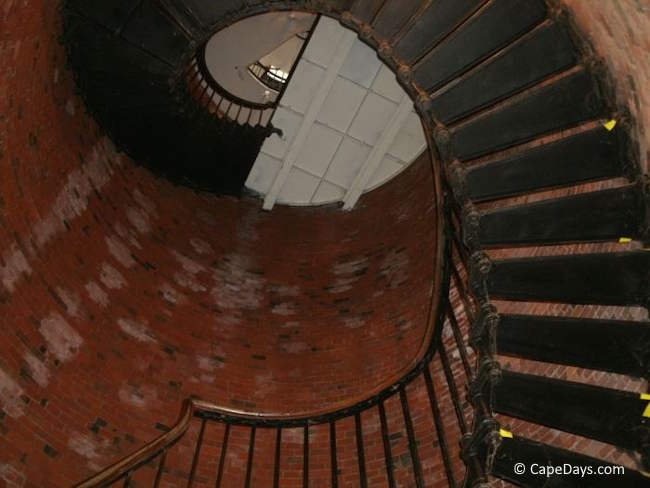 View from the base of the spiral staircase inside Highland Light, showing the brick interior walls and stairs winding upward toward the top of the tower.