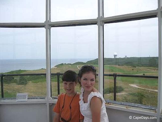 Two children sitting by the windows in the lantern room of Highland Light on Cape Cod, view of Highland Links golf course and the Atlantic Ocean in the background.