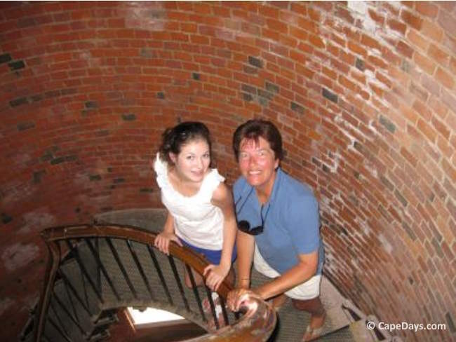 Woman and teenager partway down the spiral stairs inside Highland Light on Cape Cod, with the woman showing a nervous smile during the descent.