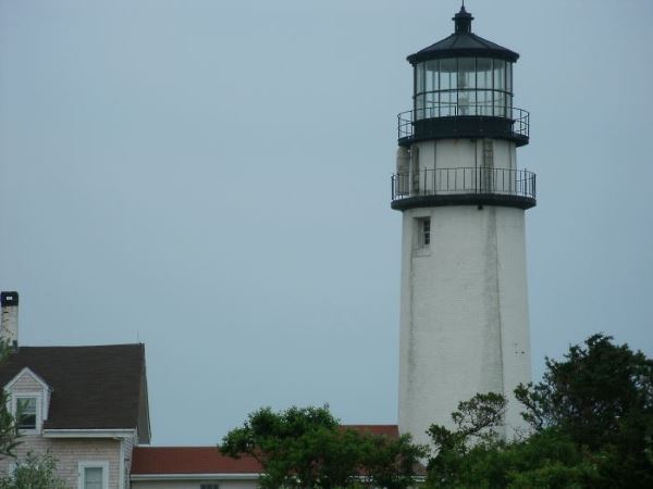 Highland Lighthouse and Keeper’s House in North Truro, with trees in the foreground and the white tower rising near the red-roofed building