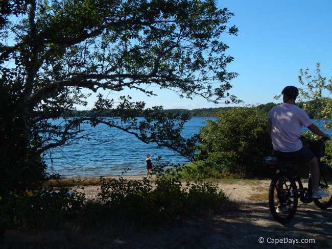 A rider pauses by Hinckley’s Pond along the Cape Cod Rail Trail in Harwich, while his wife is at the water's edge taking a photo.