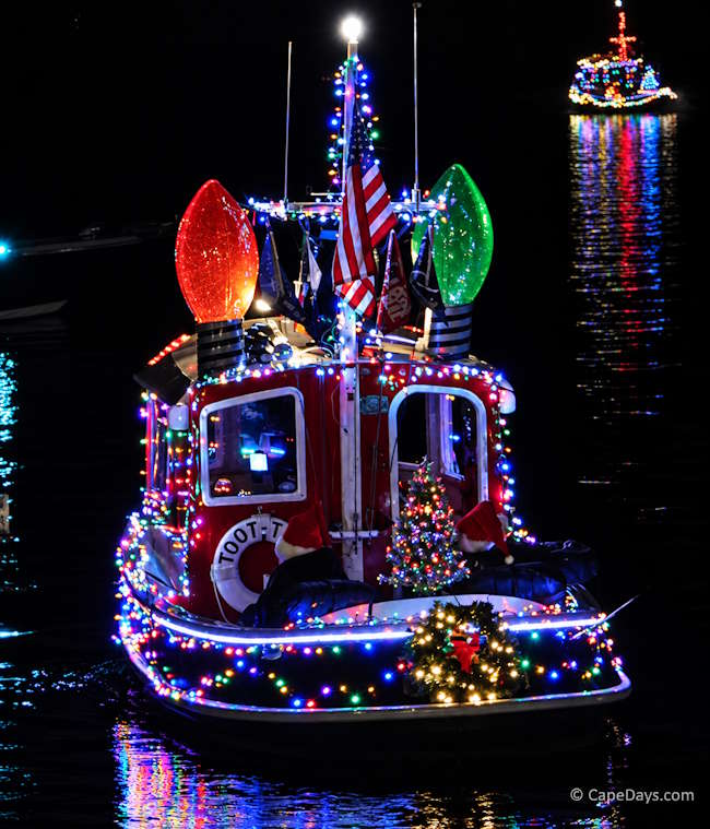 Tugboat decorated with lots of colorful lights and a small Christmas tree and wreath for the nighttime Holiday Boat Parade on Hyannis Harbor.
