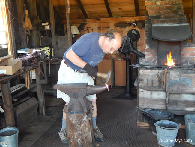 Smithy hammering a piece of red-hot iron on an anvil, inside the old blacksmith shop at Windmill Village.