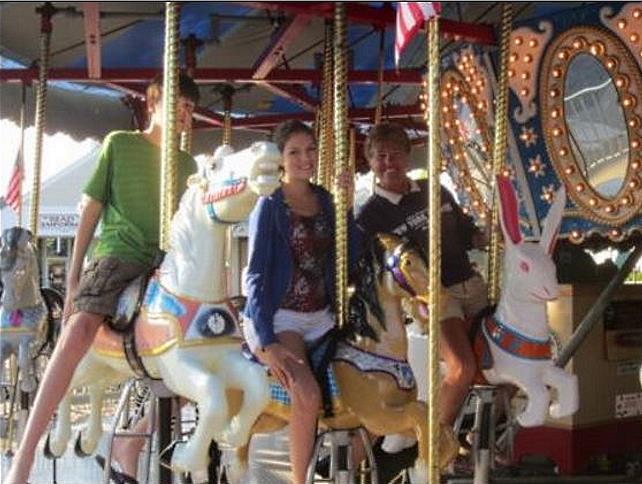 Adult and two children riding the old-fashioned carousel on Main Street in Hyannis