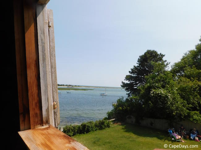 View from inside Judah Baker Windmill, looking out a window toward Bass River with visitors sitting on lawn chairs nearby. View from inside Judah Baker Windmill, looking out a window toward Bass River with visitors sitting on lawn chairs nearby.