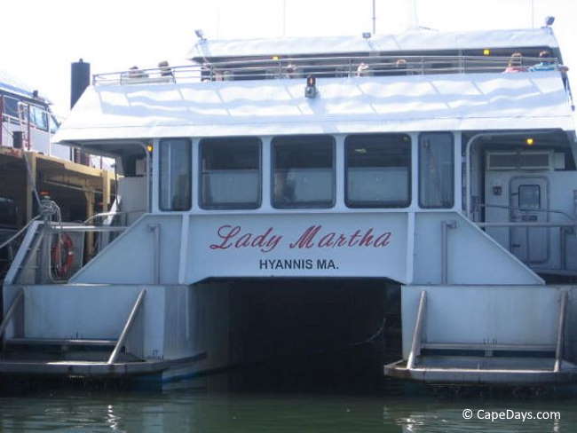 White ferry with red lettering on the stern: "Lady Martha", at the pier, passengers sitting on upper deck