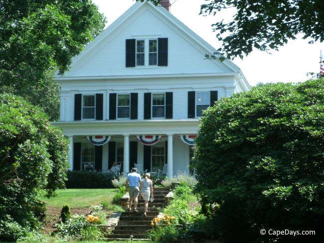 Guests walking up the garden steps to an historic white inn with black shutters and front porch in Yarmouth Port on Cape Cod.
