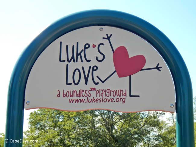Entrance sign for Luke’s Love Boundless Playground in West Barnstable, with a stick figure and big, red heart symbol
