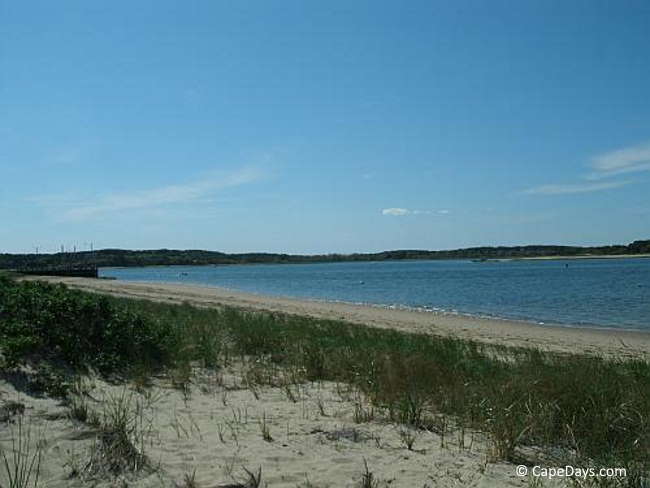 Sea grass, sand, and gentle surf lapping the shore, boats and channel markers in the distance