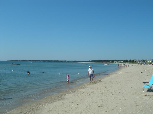 Man with a toddler at the water's edge on  a Nantucket Sound beach, family walking in the distance