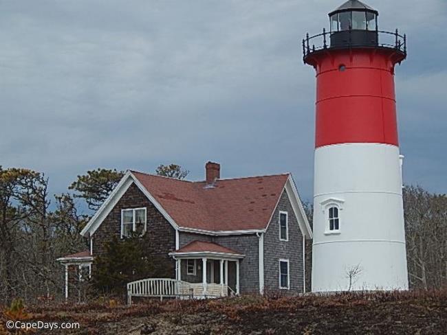 Red and white lighthouse tower alongside gray shingled keepers house with red roof.