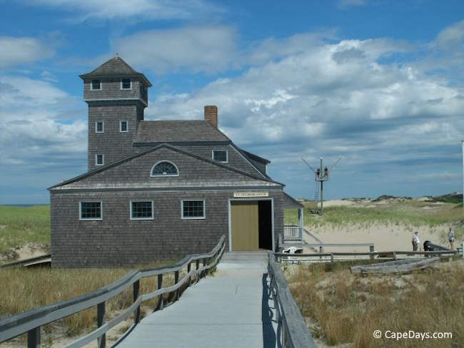 Historic life-saving station on Cape Cod with dunes in the background and boardwalk leading to the building