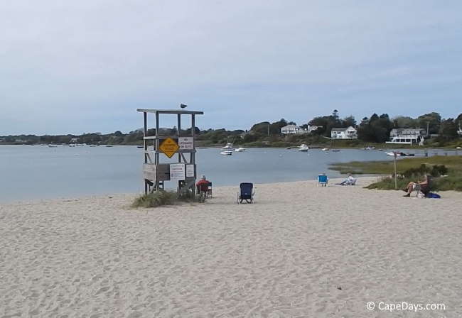 Lifeguard stand on a nearly-empty beach, boats and houses in the distance