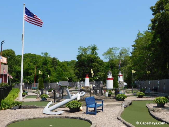 Poit's Lighthouse minigolf course with three lighthouses, several holes, a blue bench, large anchor and USA flag in view