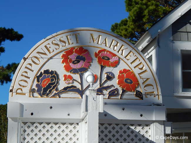 Large white sign featuring red, pink and brown poppies, gold lettering "Popponesset Marketplace"