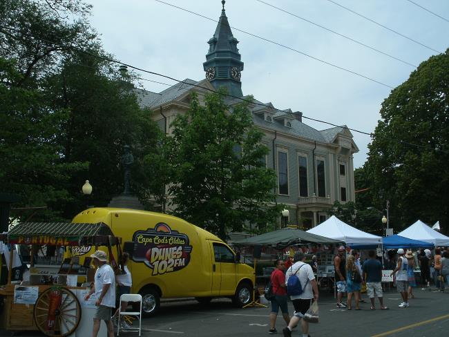 People milling around vendor tents and a yellow music bus during a festival in downtown Provincetown MA