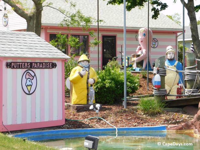 Two pink-and-white striped buildings at Putter’s Paradise, with the course-name sign and colorful statues of a pink octopus and two fishermen in view.
