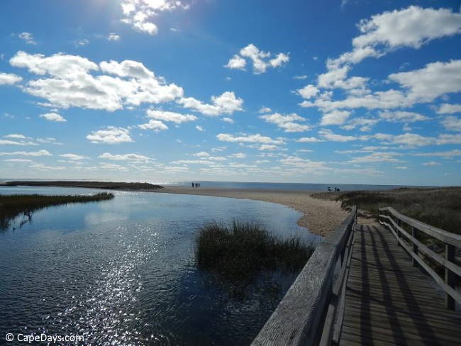 Wooden walkway over a creek, leading to an expanse of sand and ocean views