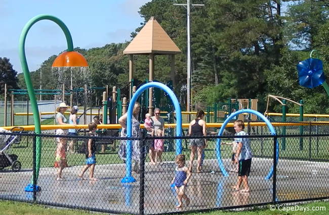 Kids playing at a splash pad as adults watch from the sidelines