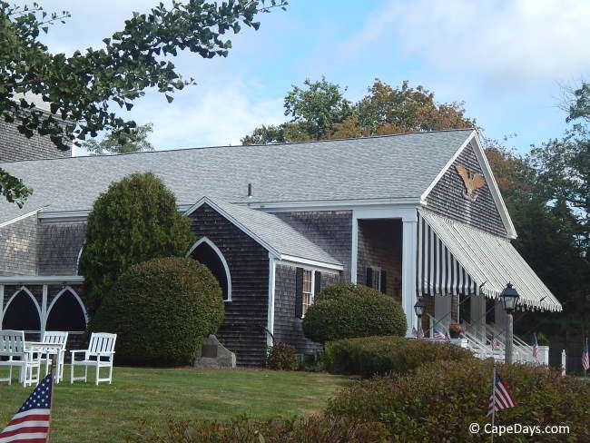 Exterior of the Cape Playhouse in Dennis, a historic shingle-style summer theater building with a striped awning and landscaped grounds.