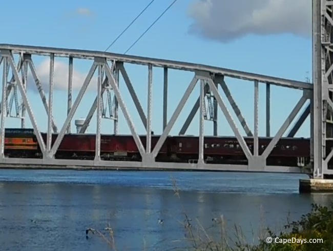 Train crossing the Cape Cod Canal on the railroad bridge, lift span lowered, viewed from the Cape-side embankment