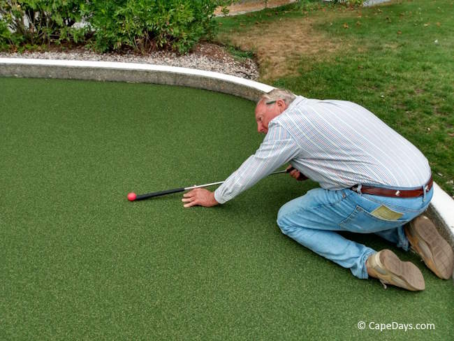 Man attempting trick shot with grip end of putter at Wild Animal Lagoon mini golf course.