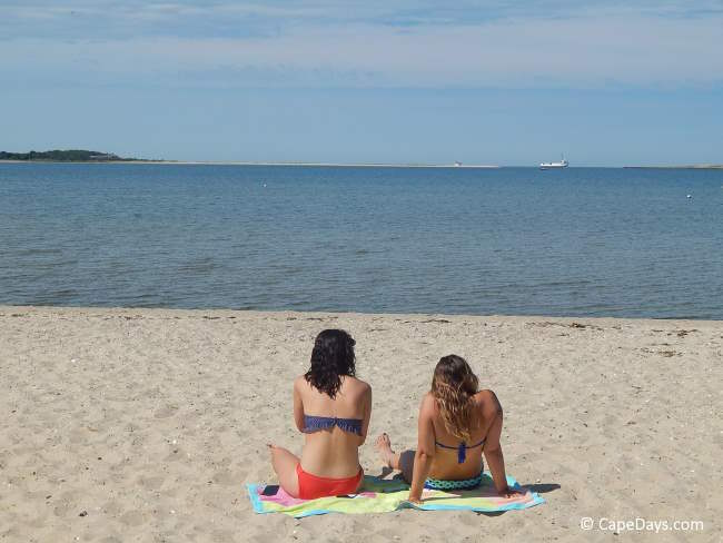 Two young women in swimsuits, sitting on a quiet stretch of beach on a clear, sunny day Two young women in swimsuits, sitting on a quiet stretch of beach on a clear, sunny day