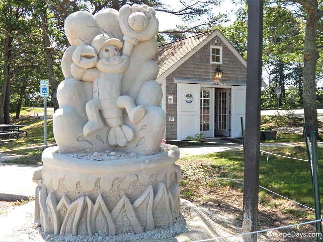 Large sand sculpture showing a cartoonish lobster dressed in baseball gear catching a ball